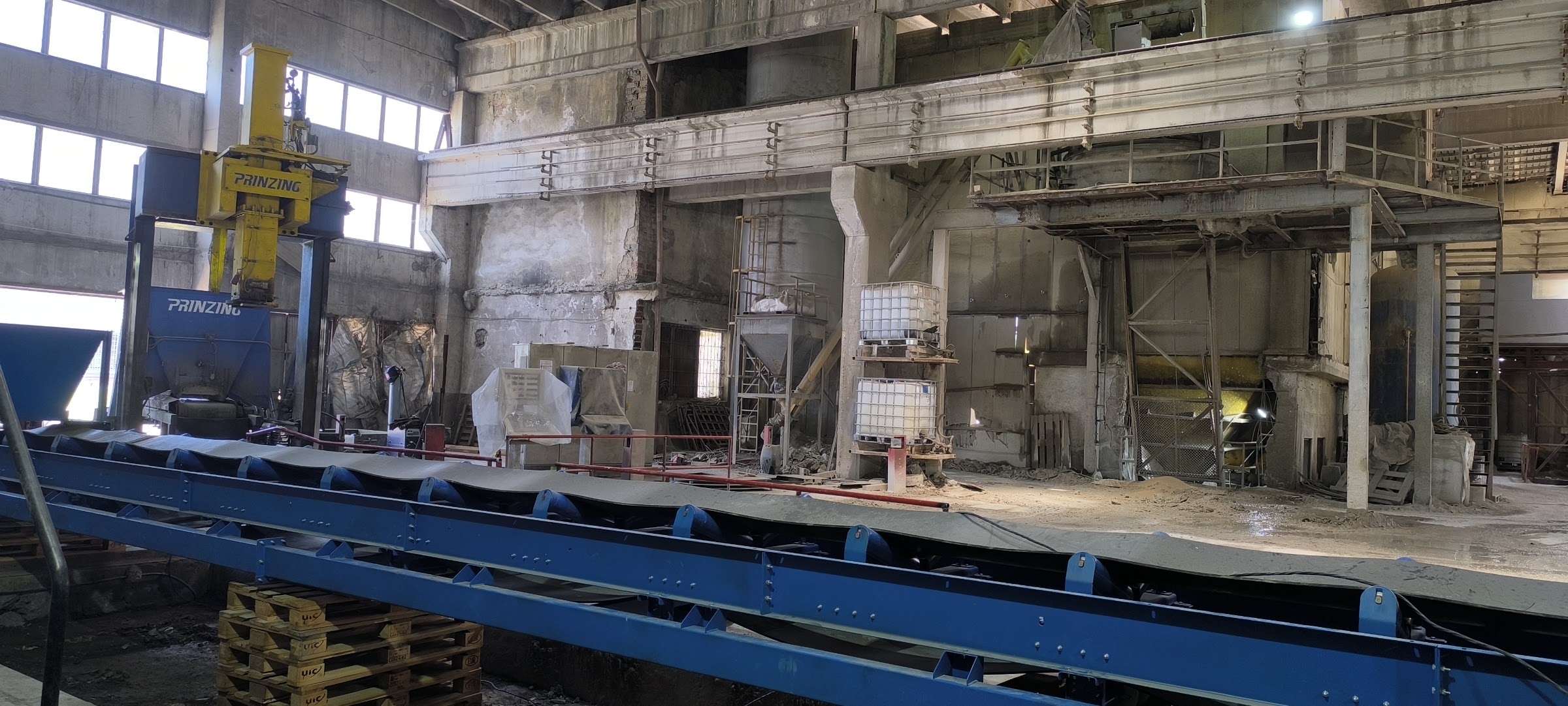 Дълъг лентов транспортьор с приемен бункер преди монтаж в производствено хале